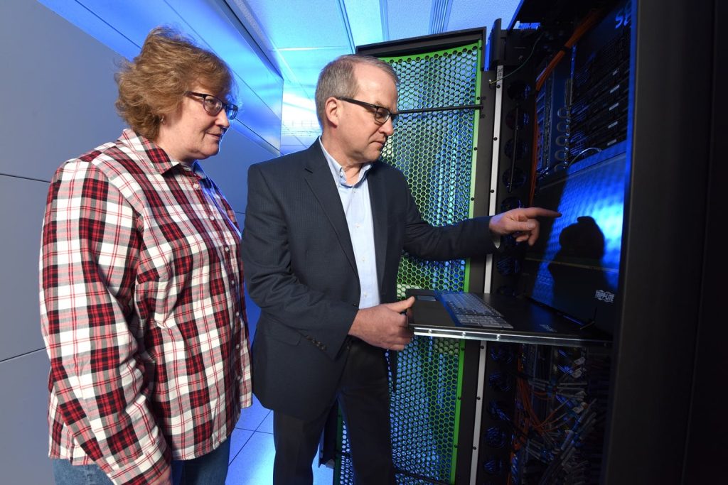two people looking at a laptop in a server room