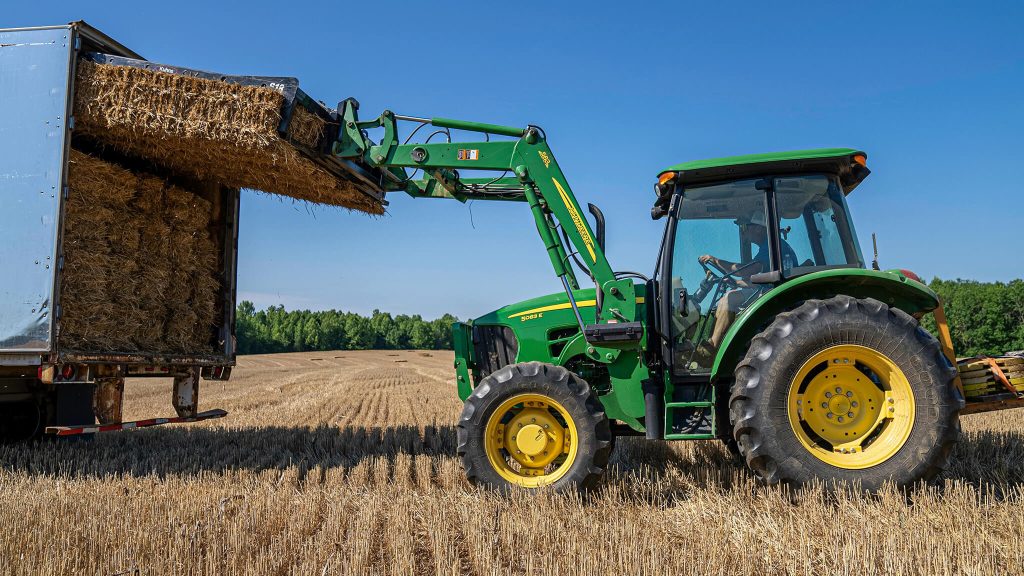 tractor loading hay bales into transport truck