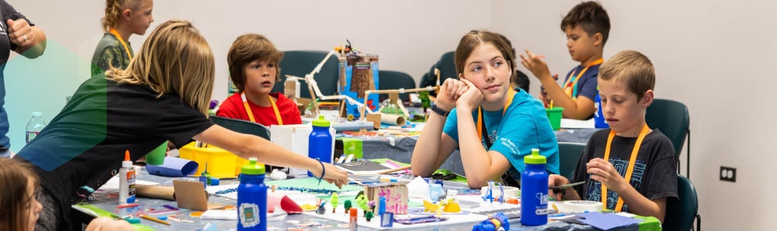 Kids working together on creative STEM projects at a craft-filled classroom table.