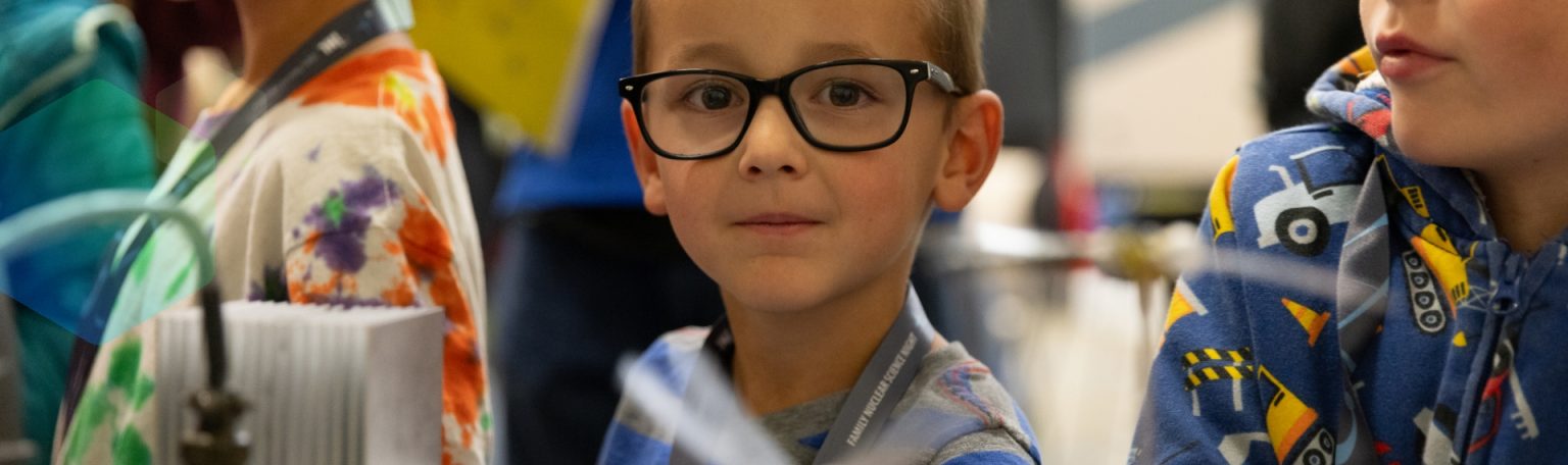 Young child wearing glasses looking at the camera during a STEM activity.