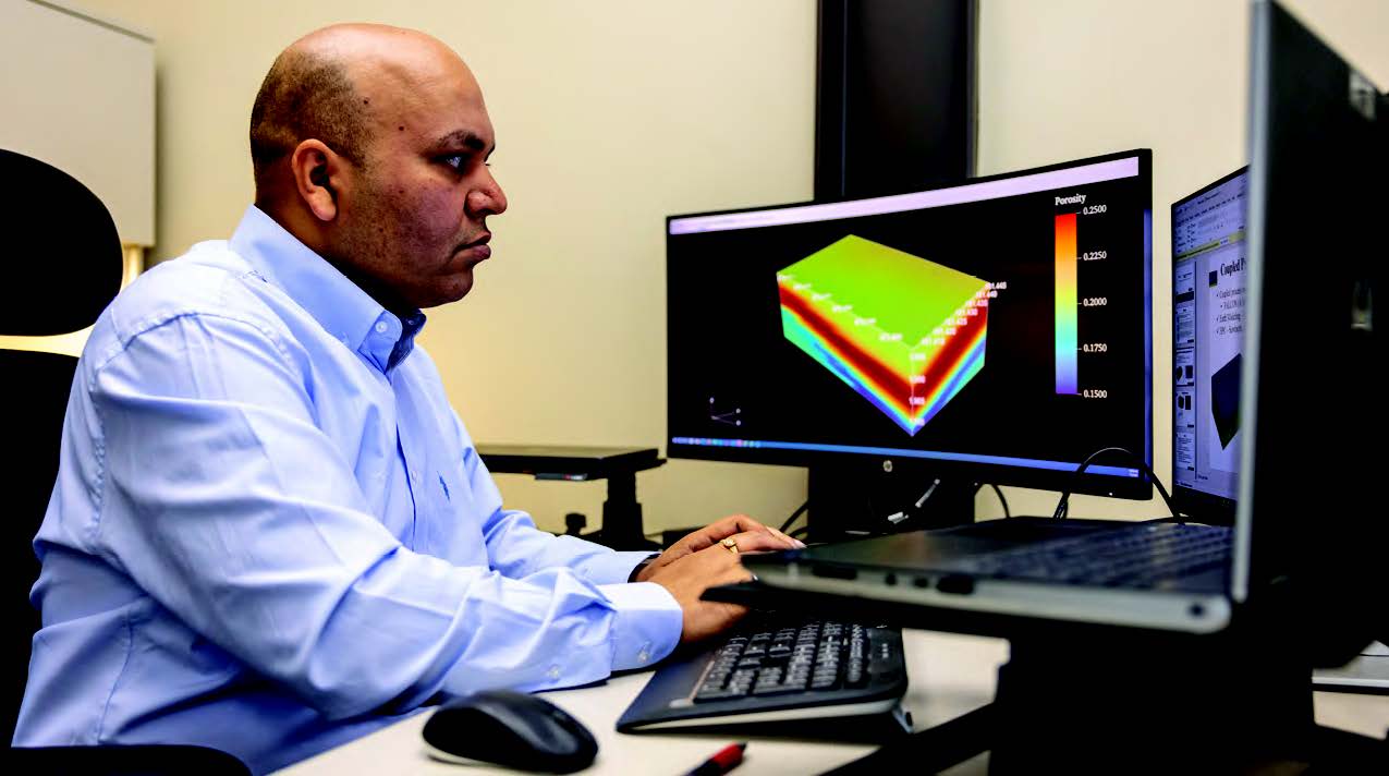Person working at a computer analyzing a 3D geoscience model on a monitor.
