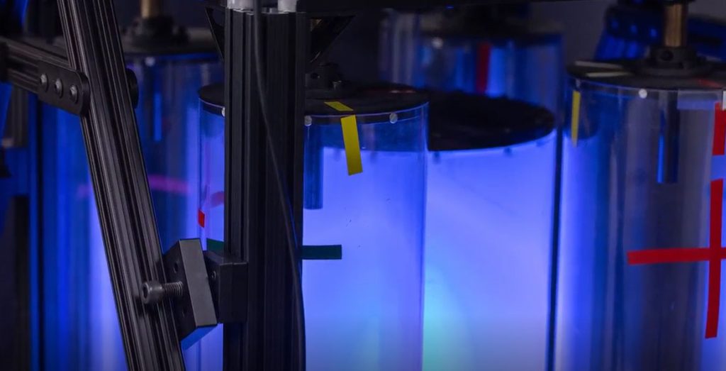 Close-up of illuminated laboratory test chambers with instrumentation and colored alignment markers.