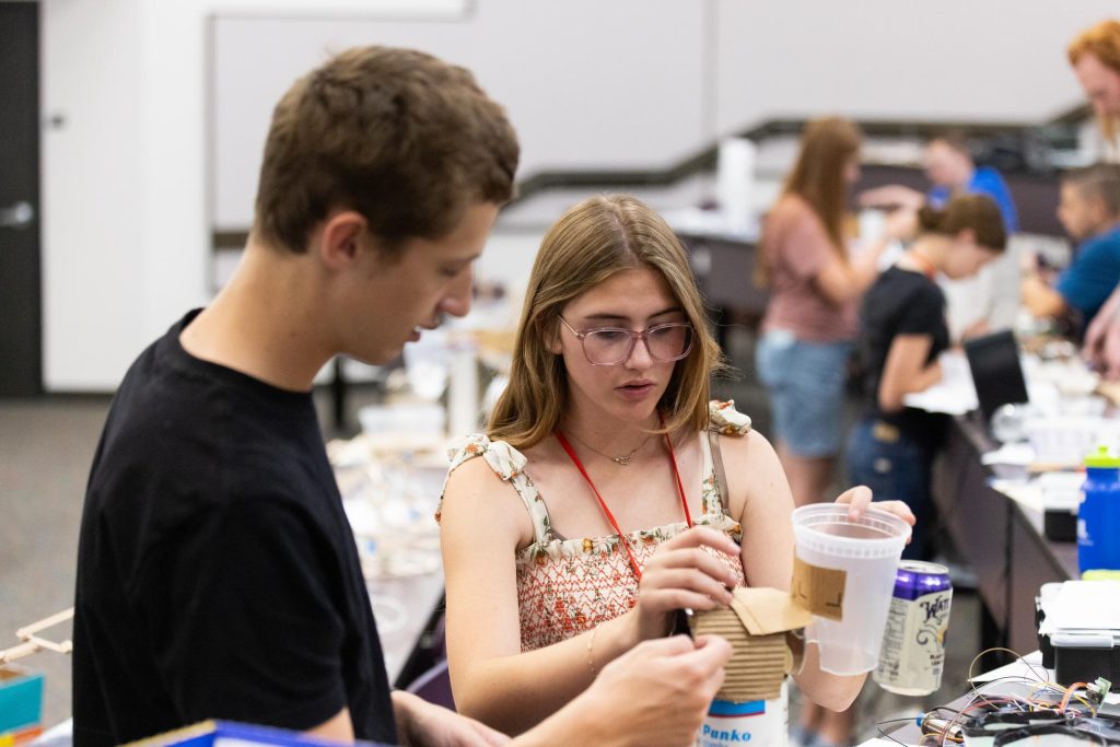 Two students working together on a small cardboard model in a classroom or lab setting.