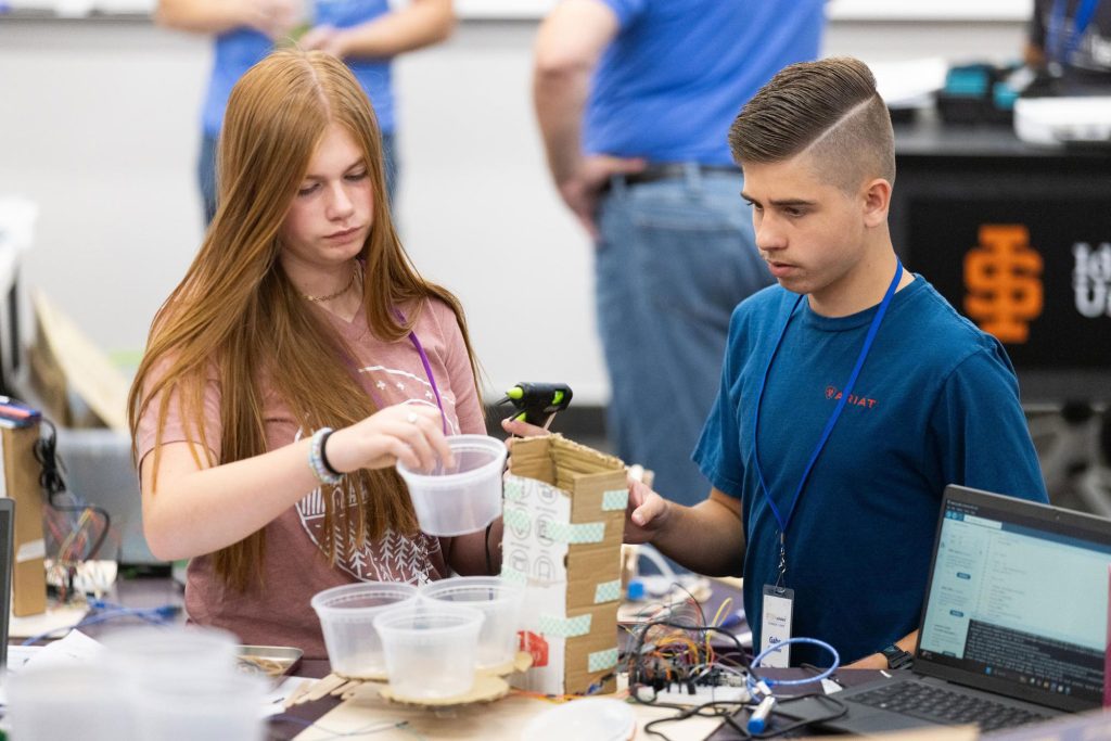 Two high school students collaborate on a hands-on STEM project with electronics and materials.