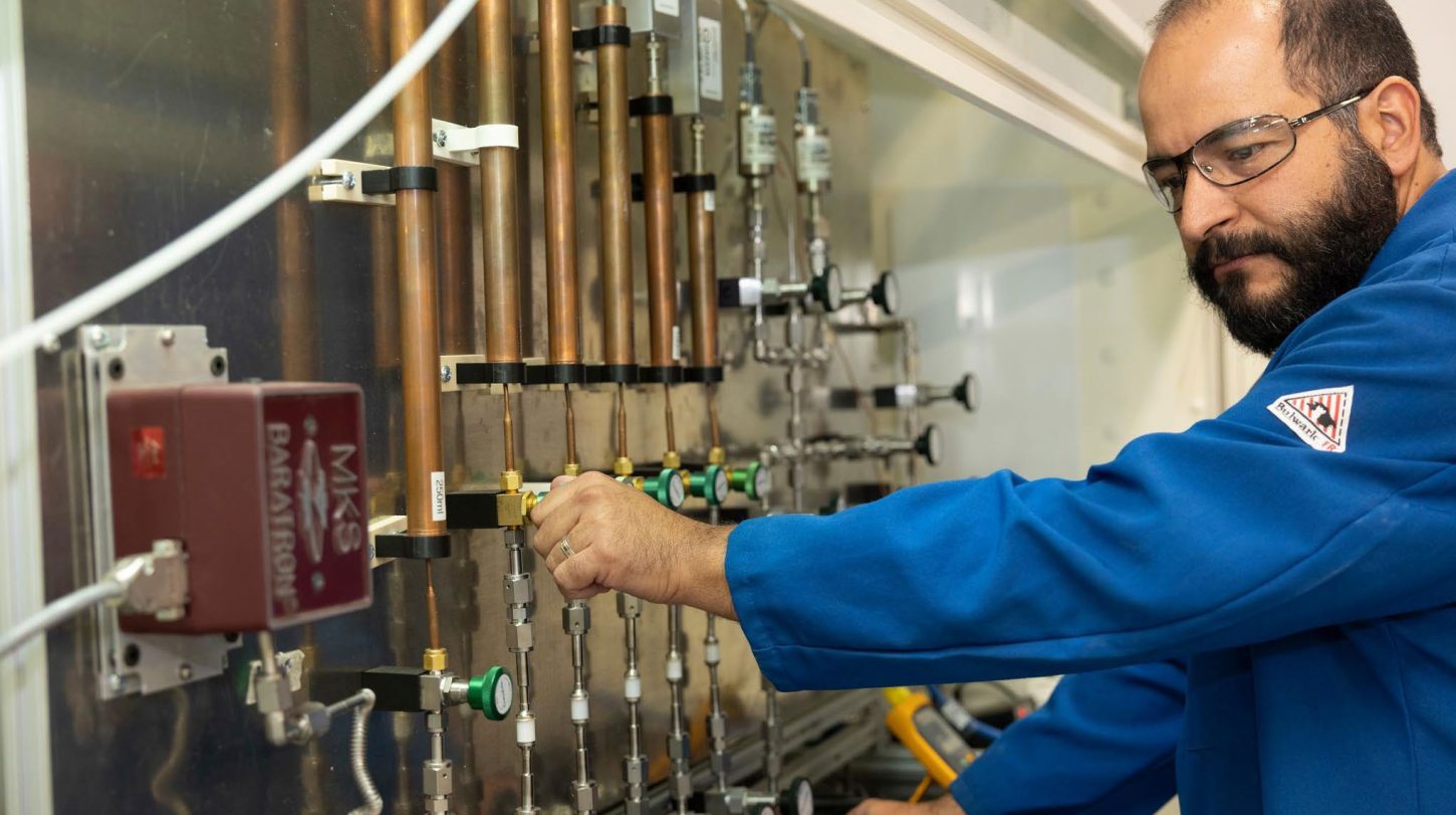 Technician adjusting valves and instruments on a laboratory gas or fluid analysis panel.