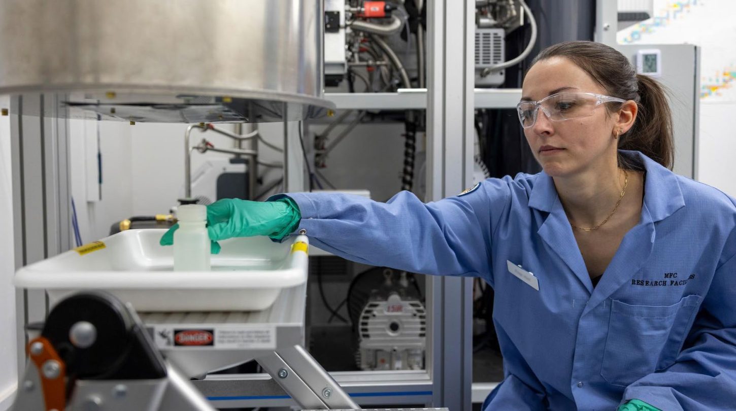 Technician in safety gear handling a sample container in a laboratory setting.