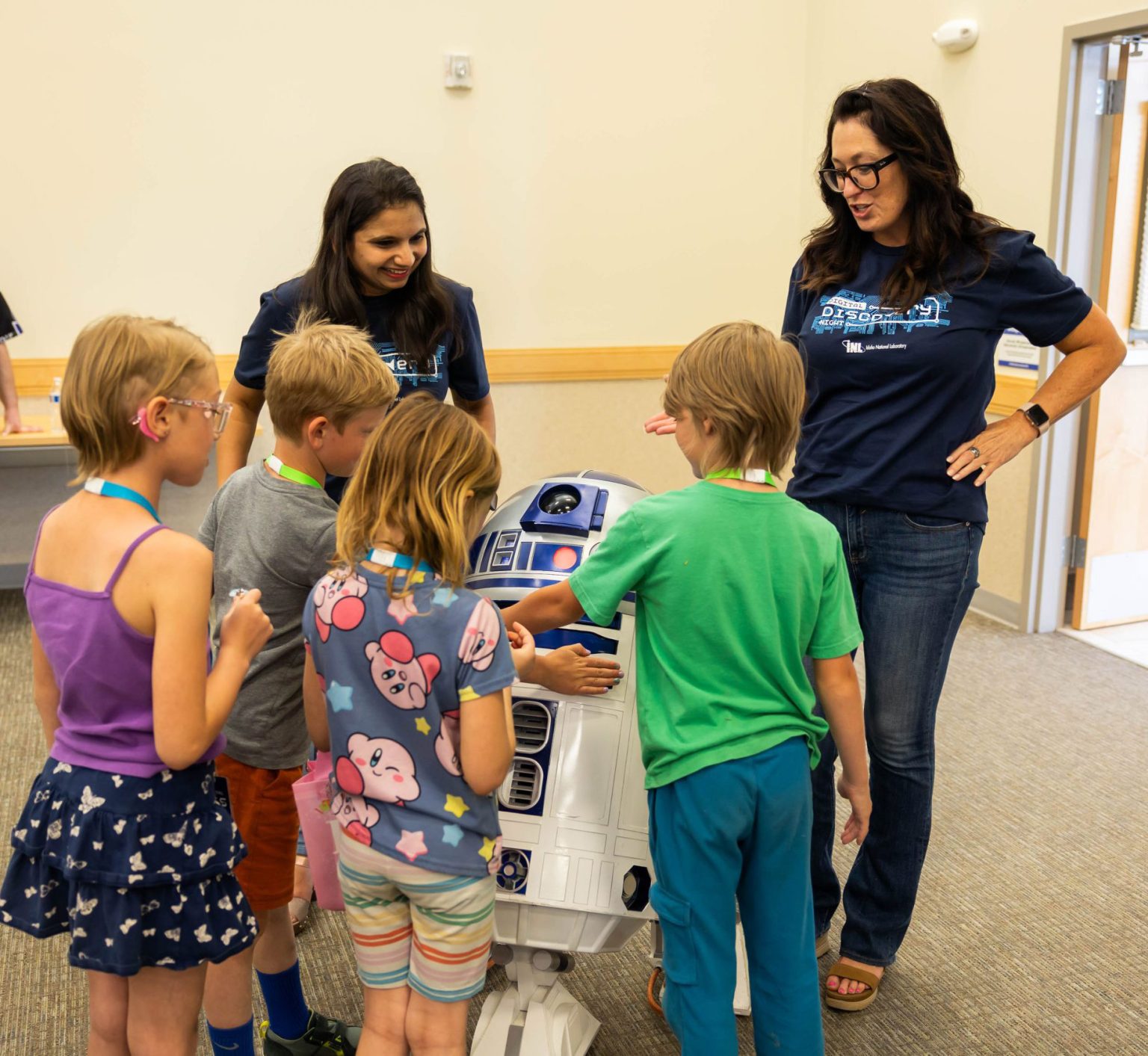 Children gathered around an R2-D2 robot with instructors during a hands-on activity.