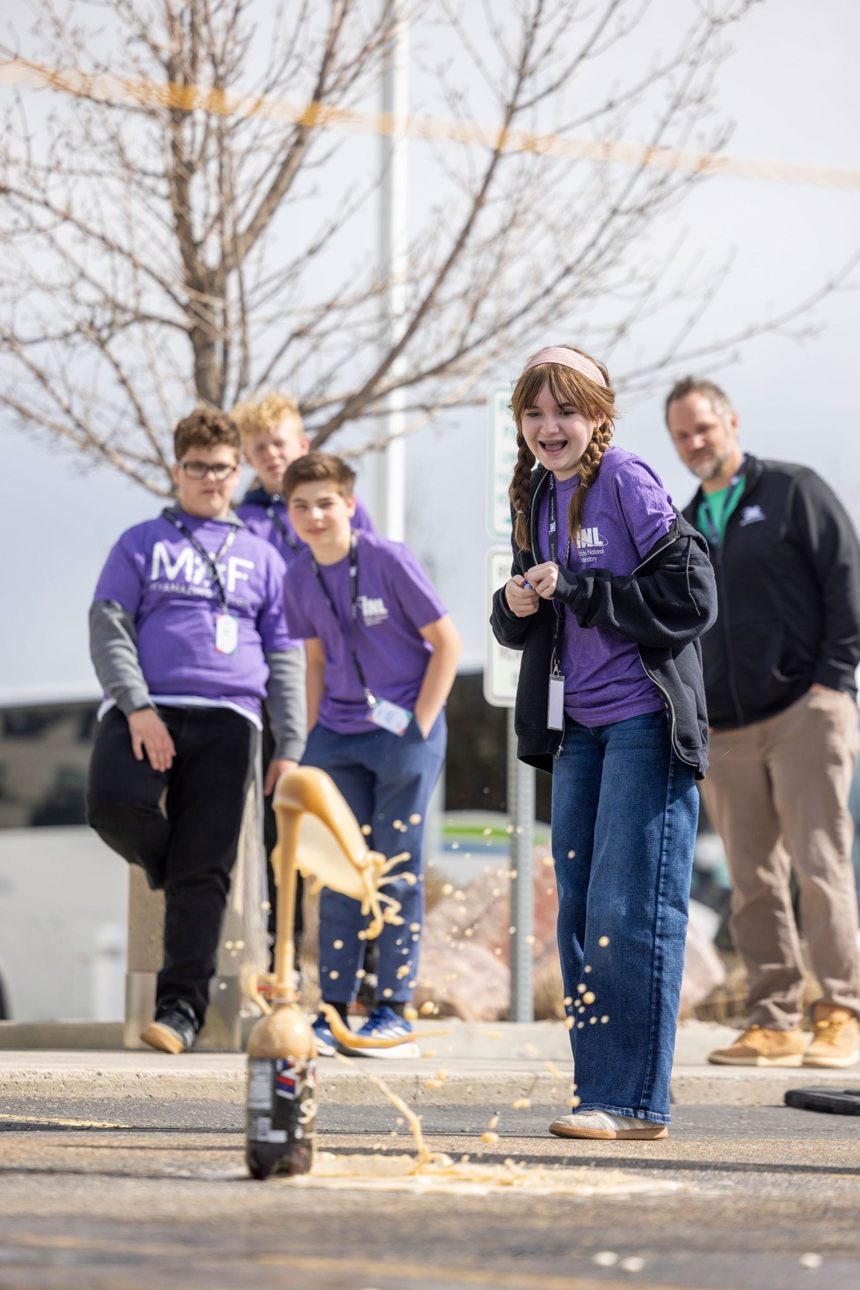Student reacting as a soda bottle erupts during an outdoor science experiment.