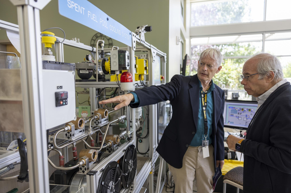 Two researchers pointing at the spent fuel pool cooling system test bench 