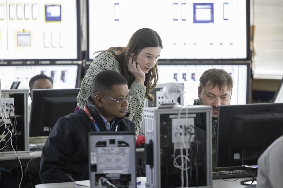 three individuals in a room with numerous computer screens