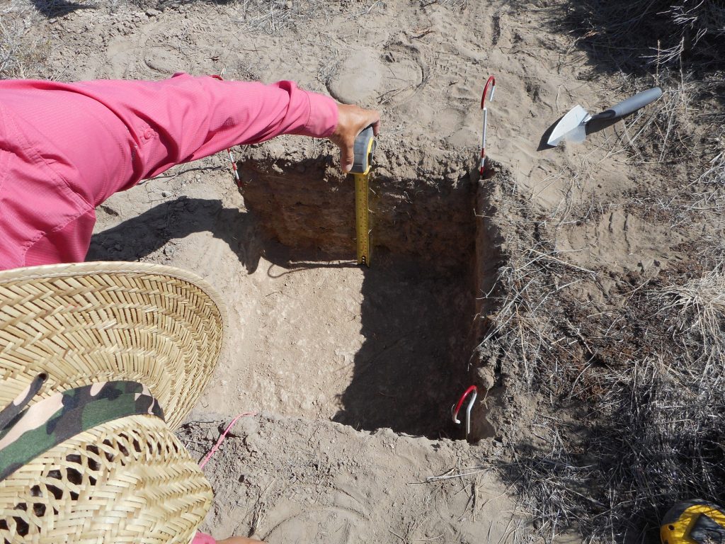 Person measuring a square space dug into the ground.