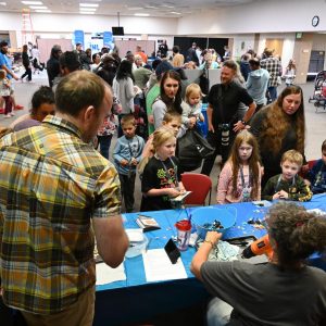 Families participate in hands-on STEM activities at a crowded community science event.