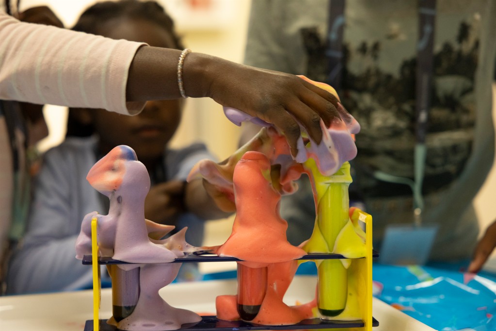 A visitor reaches toward a foam experiment at an interactive science station during the event. 